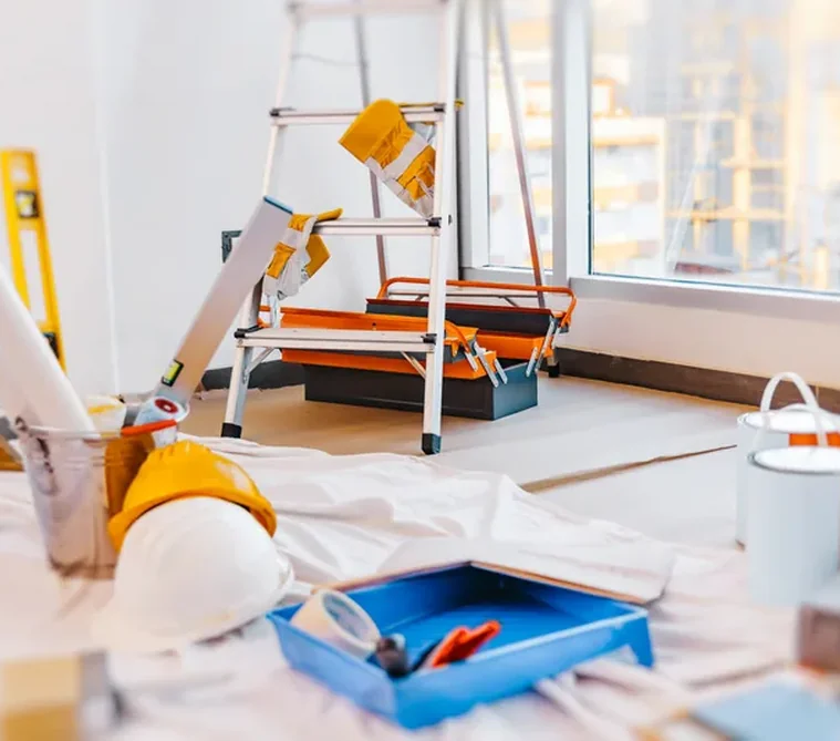 Matériel de chantier RMB+ : escabeau, bâche de protection et bac à peinture dans une pièce en travaux.