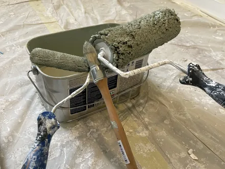 Rouleau et pinceau posés sur un bac de peinture sur un chantier protégé.
