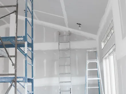 Pièce en cours de plâtrerie avec échafaudage et escabeau.