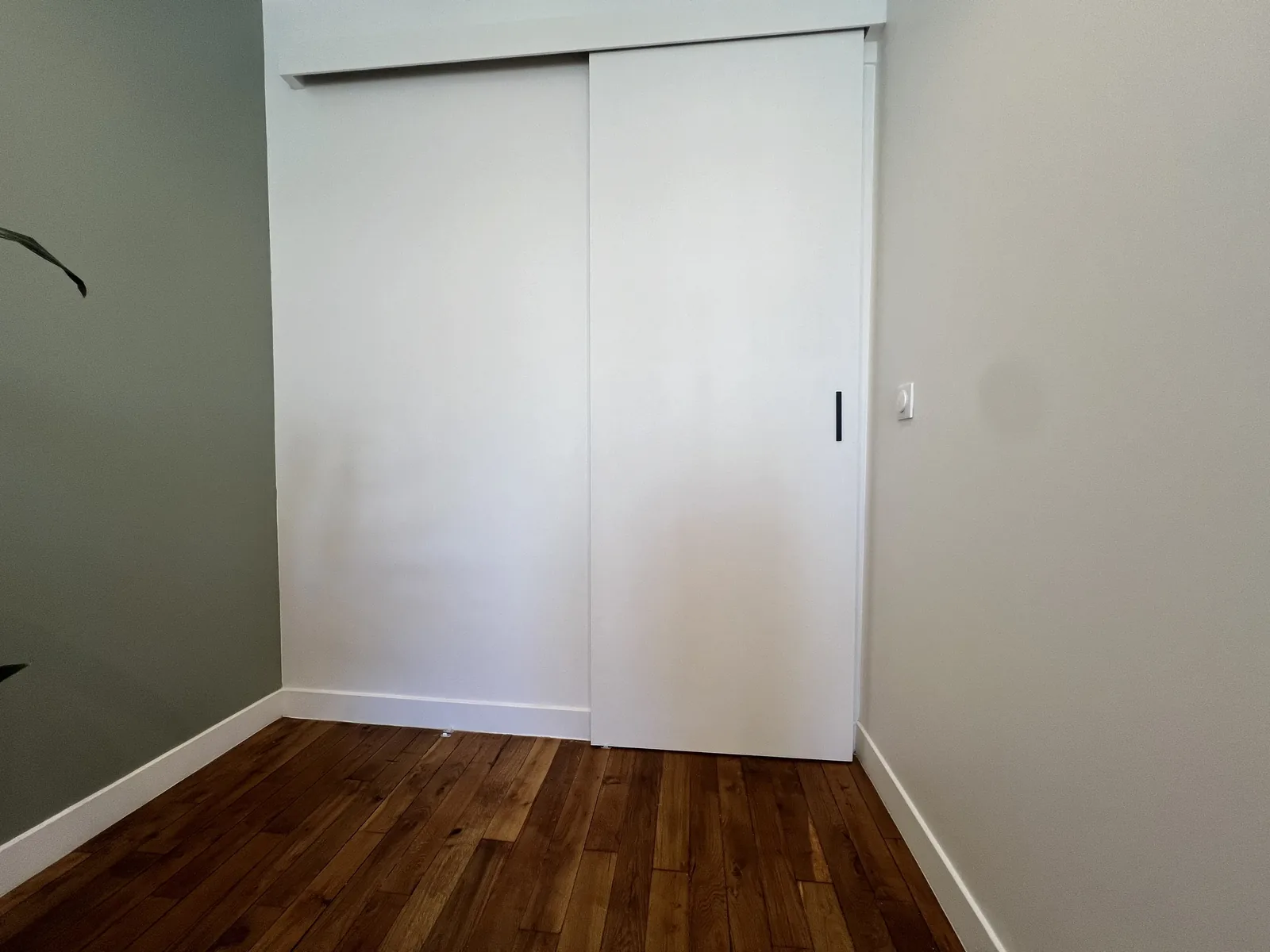 Porte coulissante blanche encastrée dans la cloison d'une chambre au parquet foncé